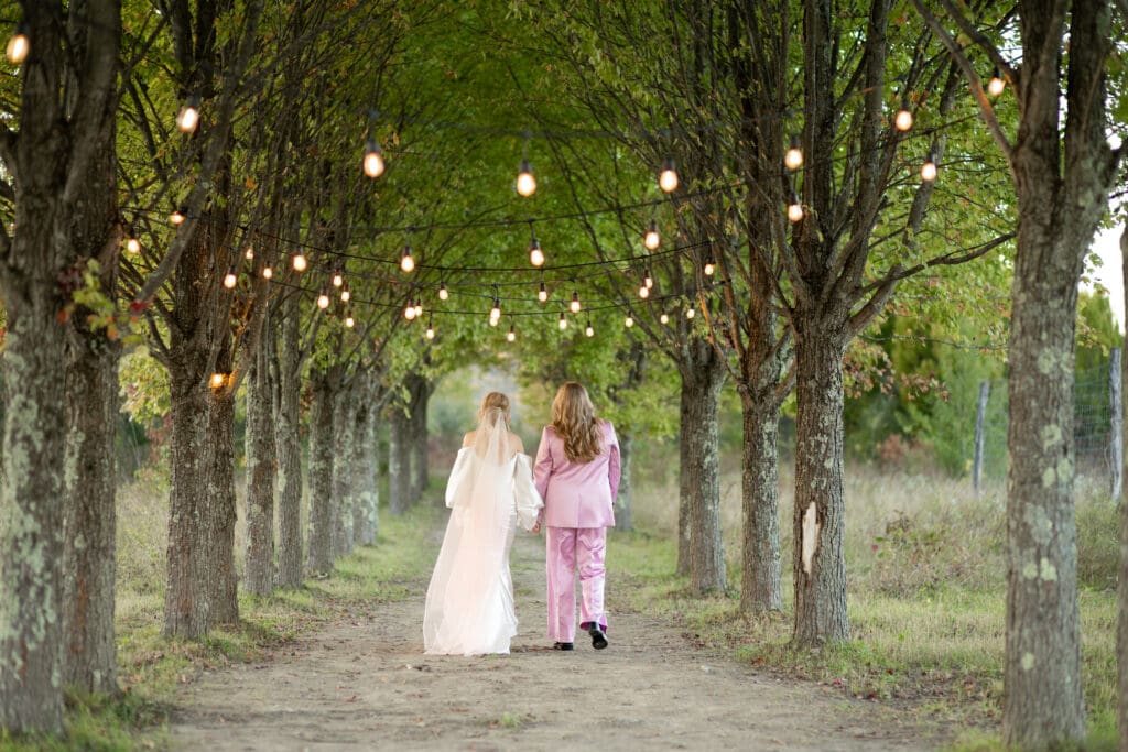 brides walk down Maple Alley hand in hand cocktail hour at Wild Flower Farms wedding in Gardiner NY